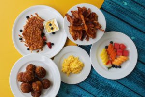 Desayuno con ensalada de frutas, tostadas francesas, tocino, huevos revueltos y muffins de guineo
