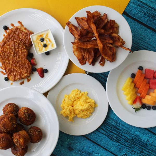 Desayuno con ensalada de frutas, tostadas francesas, tocino, huevos revueltos y muffins de guineo