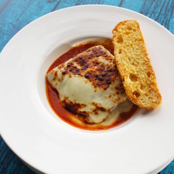Lasaña de carne con pieza de Pan en plato blanco y fondo azul