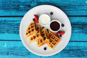 Cuatro Waffles con salsas, moras y fresas sobre plato blanco y fondo azul