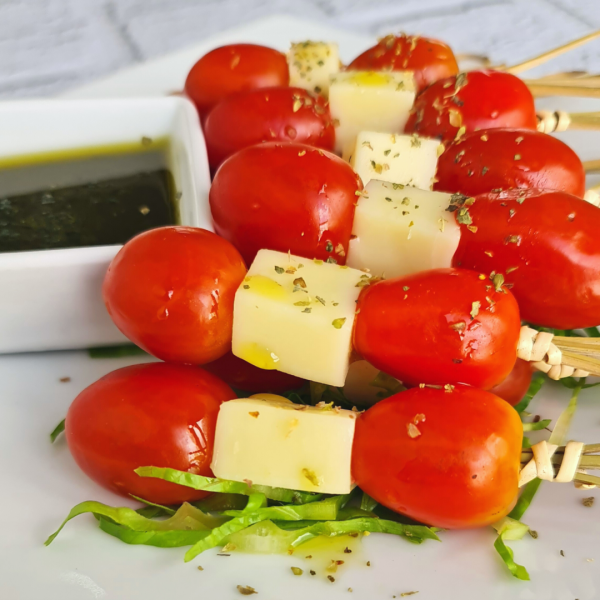 Close up de brochetas de tomate cherry y queso mozzarella con salsa chimichurri